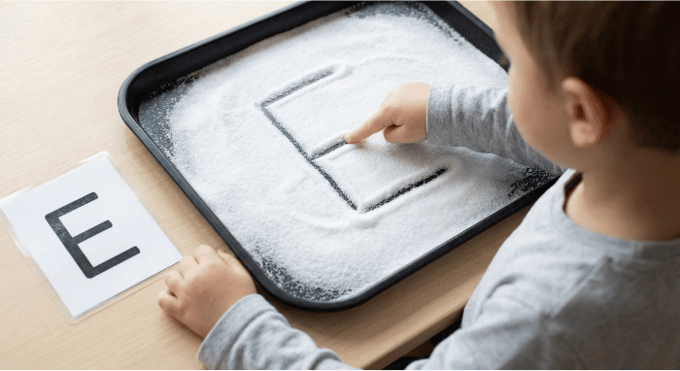 Child tracing letter E in salt tray for pre-writing practice