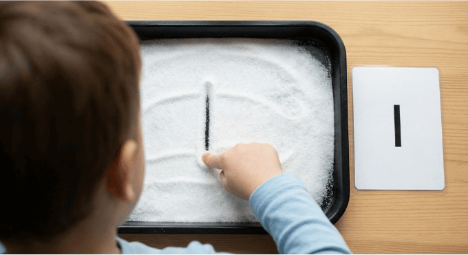 Child tracing letter I in salt tray for pre-writing practice