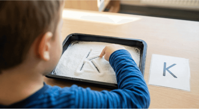 Child tracing letter K in salt tray for pre-writing practice