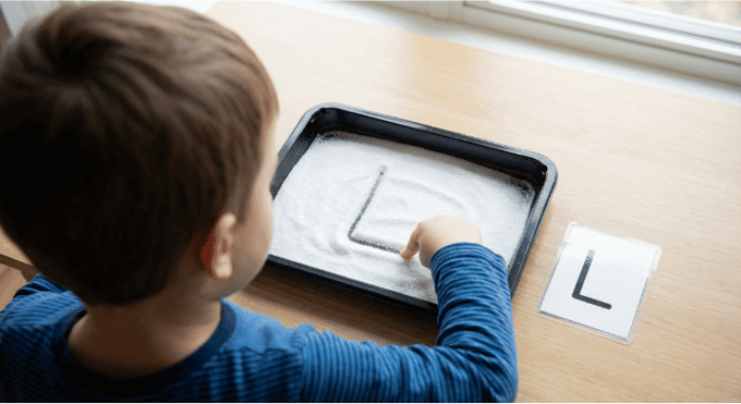 Child tracing letter L in salt tray for pre-writing practice