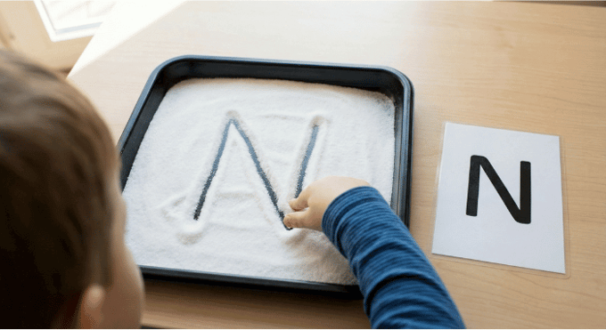 Child tracing letter N in salt tray for pre-writing practice