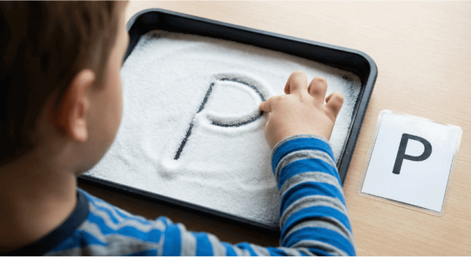 Child tracing letter P in salt tray for pre-writing practice