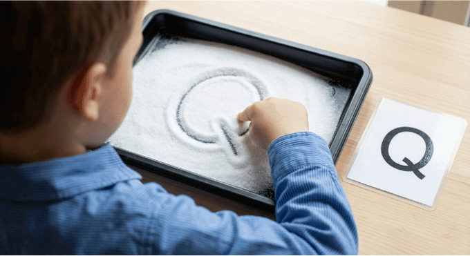 Child tracing letter Q in salt tray for pre-writing practice