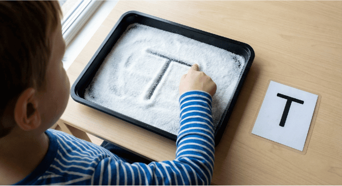 Child tracing letter T in salt tray for pre-writing practice