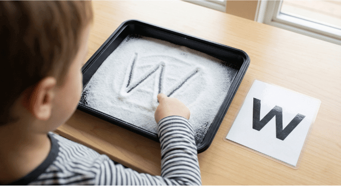 Child tracing letter W in salt tray for pre-writing practice