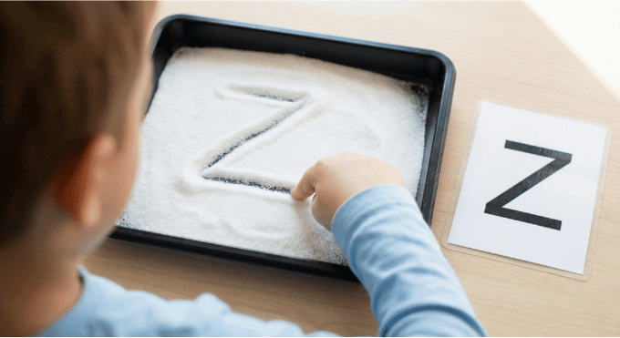 Child tracing letter Z in salt tray for pre-writing practice