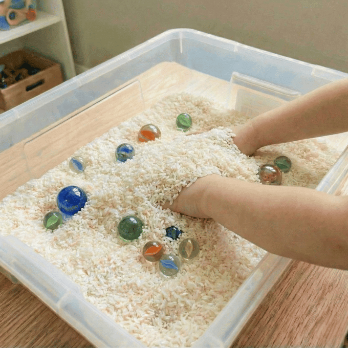 Preschool sensory bin activity with hands finding various marbles in rice
