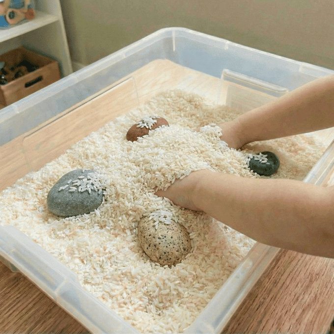 Preschool sensory bin activity with hands finding smooth rocks in rice