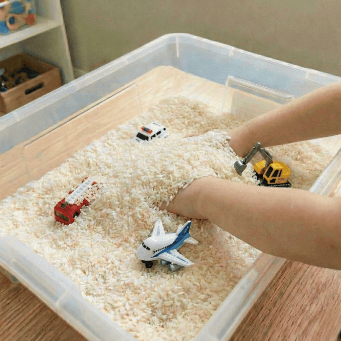 Preschool sensory bin activity with hands finding small toy vehicles in rice