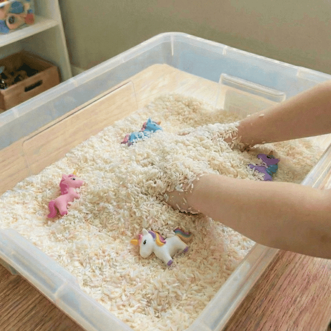 Preschool sensory bin activity with hands finding unicorn toys in rice