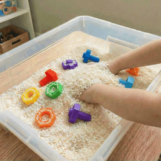 Preschool sensory bin activity with hands finding nuts and bolts in rice