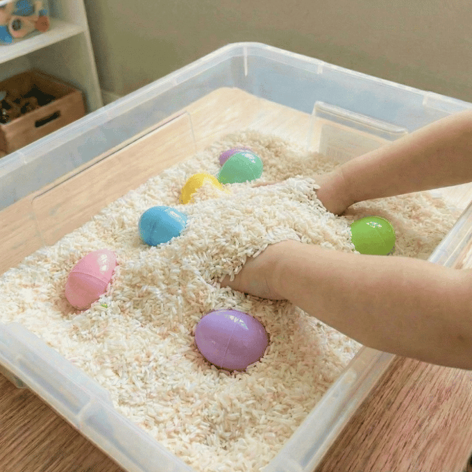Preschool sensory bin activity with hands finding small plastic easter eggs in rice