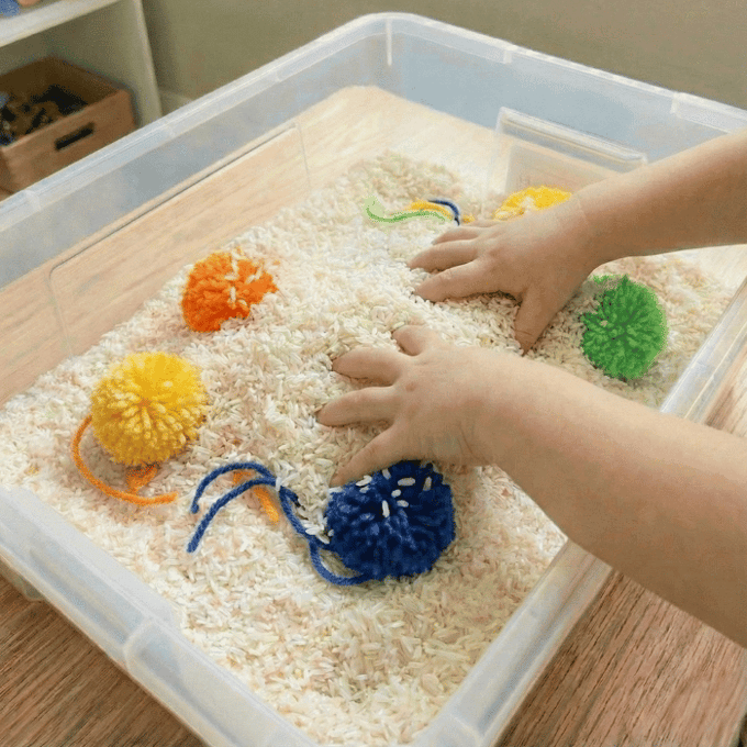 Preschool sensory bin activity with hands finding yarn balls in rice