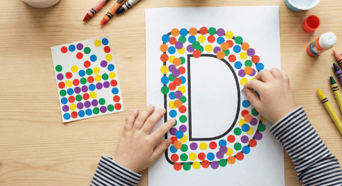 Child filling letter D outline with colorful stickers for fine motor practice