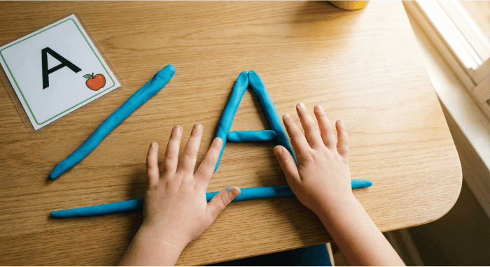 Preschooler forming letter A shape with blue playdough on table