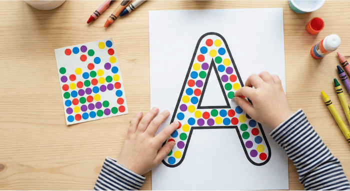 Child filling letter A outline with colorful stickers for fine motor practice