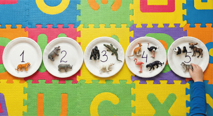 Paper plates with numbers written on them and small toy animals placed on each plate matching the quantity for active counting game