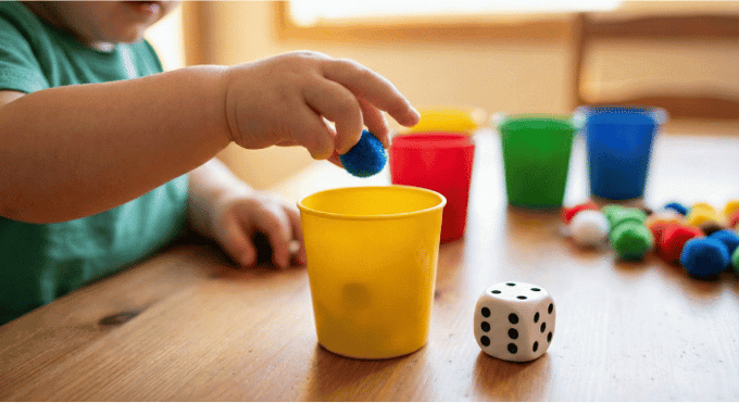 Child rolling dice and placing matching number of pom poms into cups for one-to-one correspondence practice